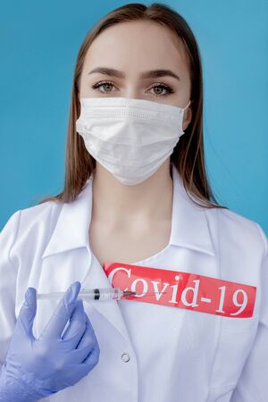 Doctor woman with surgical mask pointing to red paper with mesaage Coronavirus on blue background. World Health Organization WHO introduced new official name for Coronavirus disease named COVID-19.の写真素材
