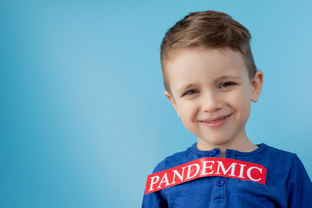 Little boy pointing to red paper with mesaage Pandemic on blue background. World Health Organization...