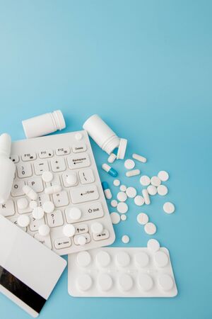 Shopping cart toy with medicaments and Keyboard. Pills, blister packs, medical bottles, thermometer, protective mask on a blue background. . Health care and internet shopping. Top view with place for your text.の写真素材