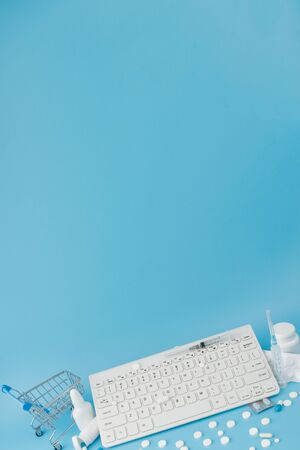 Shopping cart toy with medicaments and Keyboard. Pills, blister packs, medical bottles, thermometer, protective mask on a blue background. . Health care and internet shopping. Top view with place for your textの写真素材