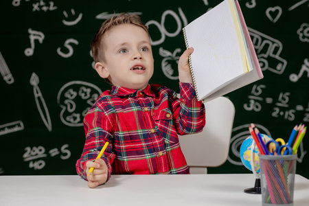 Cute child boy doing homework. Clever kid drawing at desk. Schoolboy. Elementary school student...