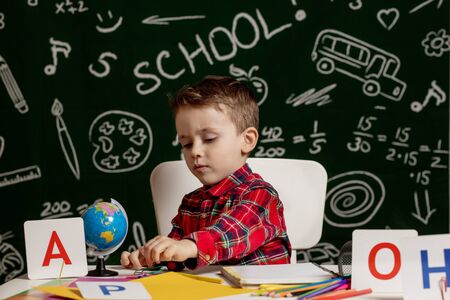 Emotional school boy sitting on the desk with many school supplies. First day of school. Kid boy from primary school. Back to school. Child from elementary schoolの写真素材