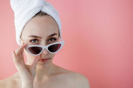 Beautiful young woman in glasses with a towel on her head after bath on pink background.の写真素材