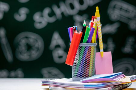 School background with stationery accessories. Books, globe, pencils and various office supplies lying on the desk on a green blackboard background.の写真素材