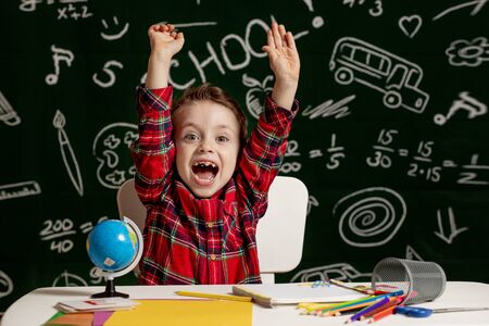 Emotional school boy sitting on the desk with many school supplies. First day of school. Kid boy from primary school. Back to school. Child from elementary schoolの写真素材