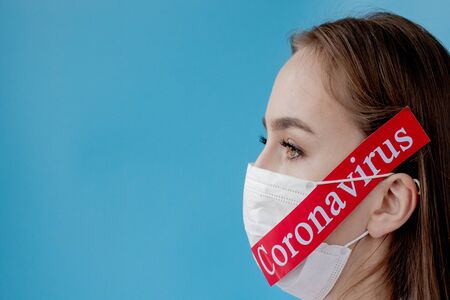 Doctor woman with surgical mask pointing to red paper with mesaage Coronavirus on blue background. World Health Organization WHO introduced new official name for Coronavirus disease named COVID-19.の写真素材