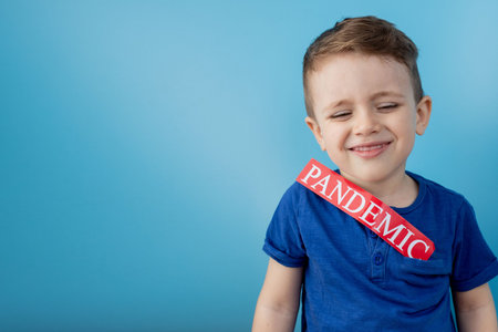 Little boy pointing to red paper with mesaage Pandemic on blue background. World Health Organization...