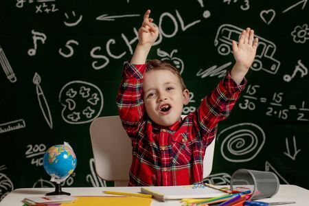 Emotional school boy sitting on the desk with many school supplies. First day of school. Kid boy from primary school. Back to school. Child from elementary schoolの写真素材