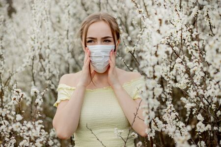 Girl in a medical mask. Girl in the spring among the blooming garden. A girl in a protective medical mask. Spring allergy concept.の写真素材