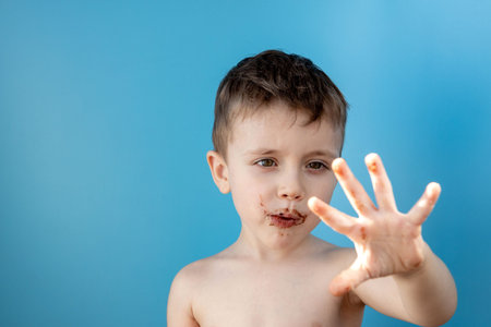 Little boy eating donut chocolate on blue background. Cute happy boy smeared with chocolate around his mouth. Child concept, tasty food for kids.の写真素材