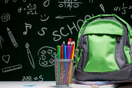 Education concept - green backpack, notebooks and school supplies on the background of the blackboard.の写真素材