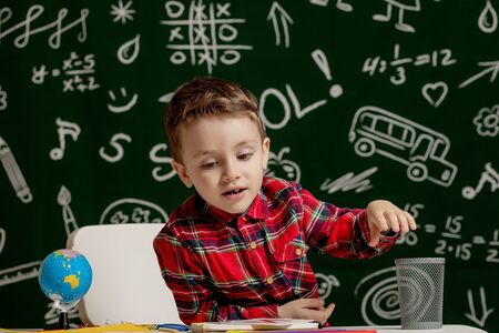 Emotional school boy sitting on the desk with many school supplies. First day of school. Kid boy from primary school. Back to school. Child from elementary schoolの写真素材
