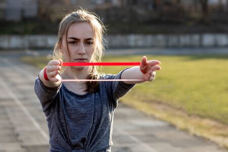 Young slim woman in sportswear doing squats exercise with rubber band on a black coated stadium track.の写真素材