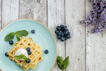 Fresh baked homemade classic Belgian waffles topped with icecream, fresh blueberries and mint on wooden background, top down view. Savory waffles. Breakfast concept.の写真素材
