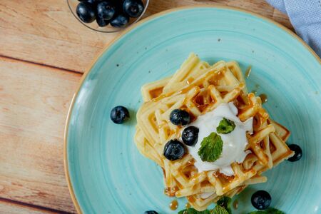 Fresh baked homemade classic Belgian waffles topped with icecream, fresh blueberries and mint on wooden background, top down view. Savory waffles. Breakfast concept.の写真素材