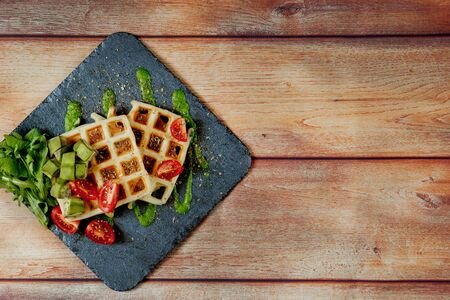Fresh baked Belgian waffles with arugula, tomatoes and avocado on black a plate. Savory waffles. Breakfast concept. Healthy breakfast.の写真素材