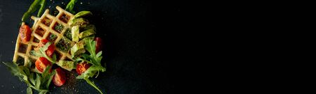 Fresh baked Belgian waffles with arugula, tomatoes and avocado on black a plate. Savory waffles. Breakfast concept. Healthy breakfast.の写真素材