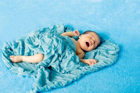 Newborn 14 day old baby boy lying on his back crying on blue wrap cloth.の写真素材