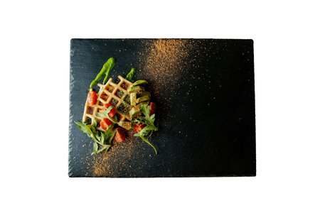 Fresh baked Belgian waffles with arugula, tomatoes and avocado on black a plate isolated on white background. Savory waffles. Breakfast concept. Healthy breakfast.の写真素材