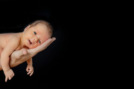 Father holding his 15 days old son in his hand on black background.