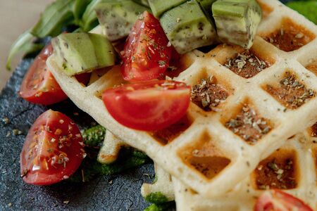 Fresh baked Belgian waffles with arugula, tomatoes and avocado on black a plate. Savory waffles. Breakfast concept. Healthy breakfast.の写真素材