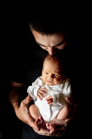 Father holding his 15 days old son in his hand on black background. Baby lying on his fatherの写真素材