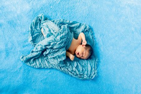 Newborn 14 day old baby boy lying on his back crying on blue wrap cloth.の写真素材