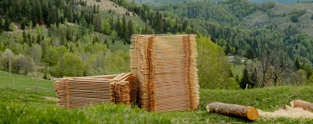 Piles of wooden boards on green grass with mountains on background, planking for construction. Wood timber stack of wooden blanks building material.の写真素材