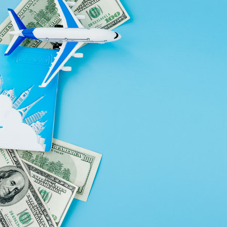 Passport with model of passenger plane and dollars on blue background. Travel concept, copy spaceの写真素材