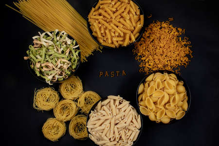 Various mix of pasta on dark background, metal spoons. Food concept. the word pasta Italian food and menu concept.の写真素材