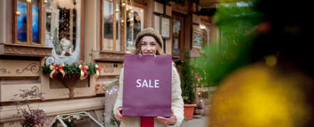 Happy girl holds paperbags with symbol of sale in the stores with sales at Christmas, around the city. Concept of shopping, holidays, happiness, Christmas Salesの写真素材
