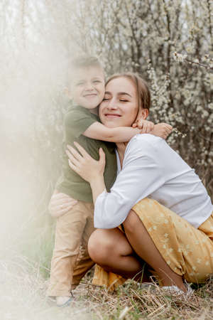 Happy mother and son having fun together. Mother gently hugs her son. In the background white flowers bloom. Mother's day.の写真素材