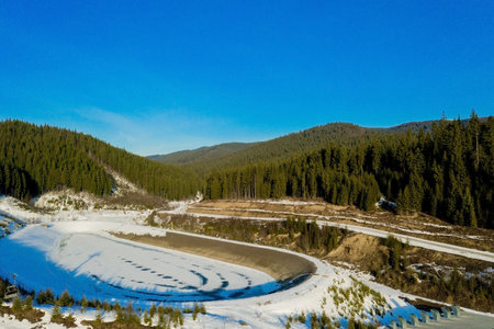 Aerial view of landscape of ski and snowboard slopes through pine trees going down to winter resort...