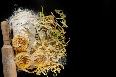 Freshly cooked pasta is lying on a dark surface dusted with flour. Italian pasta. Tagliatelle. Raw pasta. Italian pasta recipe. Top view, copy space.の写真素材