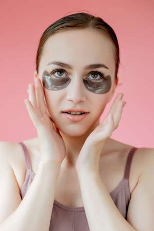 Head shot portrait close up smiling young woman with under eye moisturizing patches mask looking at camera enjoying skincare procedure.の写真素材