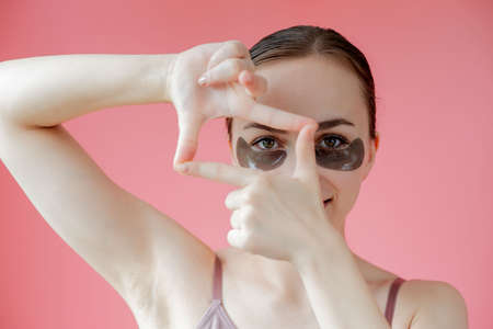 Head shot portrait close up smiling young woman with under eye moisturizing patches mask looking at camera enjoying skincare procedure.の写真素材