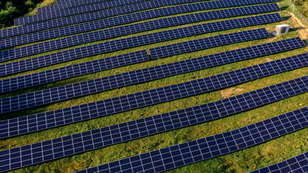 Solar Power Station in Green Field on Sunny day. Aerial view. Solar Panels Stands in a Row in Field for Power Production. Drone fly over Solar Farm. Renewable green energy. Alternative energy sourcesの写真素材