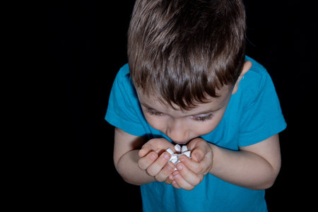 Kid holds heap of white pills and drugs in his hand palm on black background. Concept of drug...