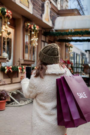 Happy girl holds paperbags with symbol of sale in the stores with sales at Christmas, around the city. Concept of shopping, holidays, happiness, Christmas Salesの写真素材