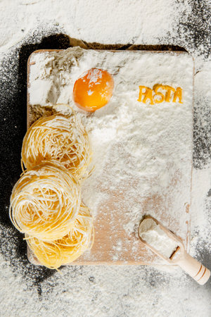 Freshly cooked pasta is lying on a dark surface dusted with flour. Italian pasta. Tagliatelle. Raw...