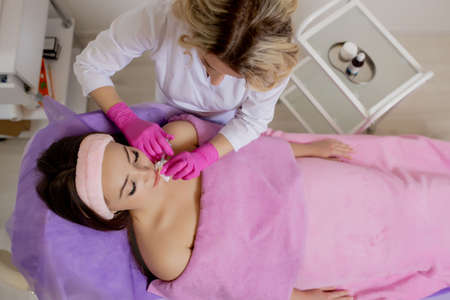 The doctor cosmetologist makes the Rejuvenating facial injections procedure for tightening and smoothing wrinkles on the face skin of a beautiful, young woman in a beauty salonの写真素材