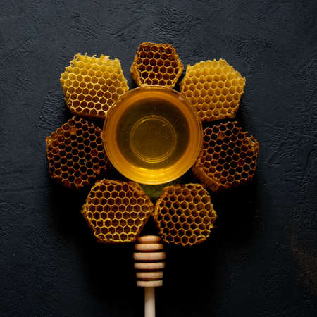 Honey and honeycomb in the form of a flower on black table, top view. space for text.の写真素材