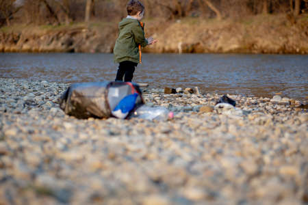 Save environment concept, a little boy collecting garbage and plastic bottles on the beach to dumped into the trash.の写真素材