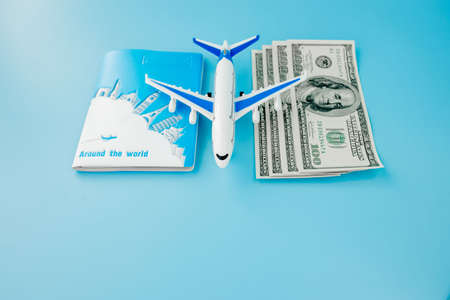 Passport with model of passenger plane and dollars on blue background. Travel concept, copy spaceの写真素材