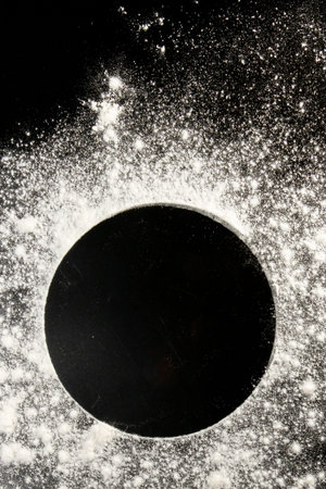 Sprinkled wheat flour circle, round spot on black. Top view on blackboard. Baking concept, cooking...