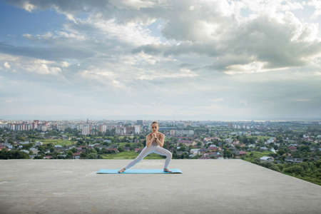 Side view of muscular young woman with long ponytail in sunny morning. Gorgeous girl practicing exercises, warming up lower body on city background.の写真素材