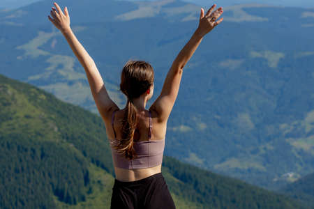 The young woman at the top of the mountain raised her hands up on blue sky background. The woman climbed to the top and enjoyed her success. Back view.の写真素材
