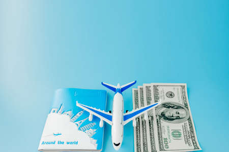 Passport with model of passenger plane and dollars on blue background. Travel concept, copy spaceの写真素材