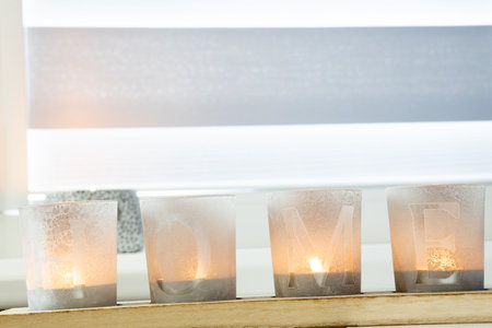 candles with the inscription HOME on the windowsill with beautiful blinds.の写真素材