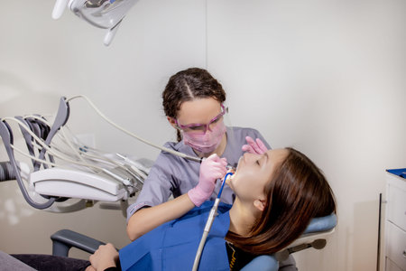Adult woman visiting a dental office. Dentist hands in rubber protective gloves using white polishing stone for patient.の写真素材